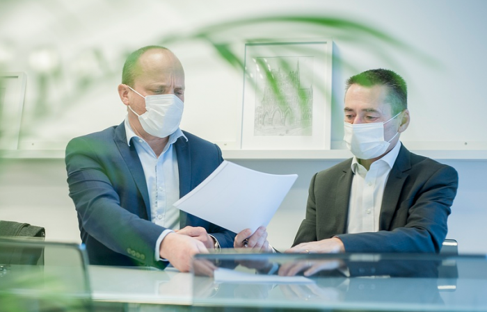 Deux hommes portant un masque de protection et signant des papiers